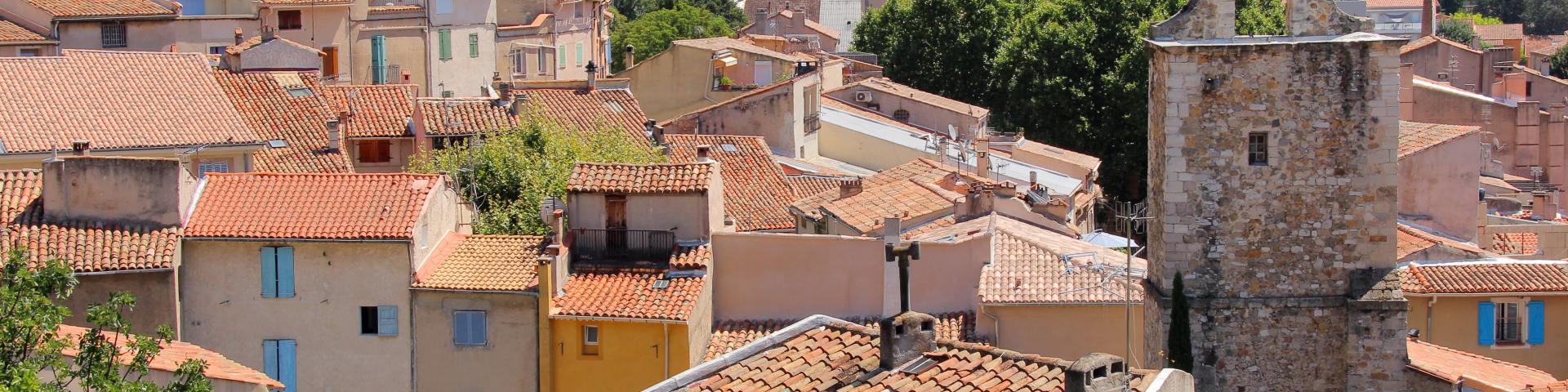 Panorama d’un village provençal d'Auriol avec toits en tuiles, tour en pierre et collines verdoyantes en arrière-plan.