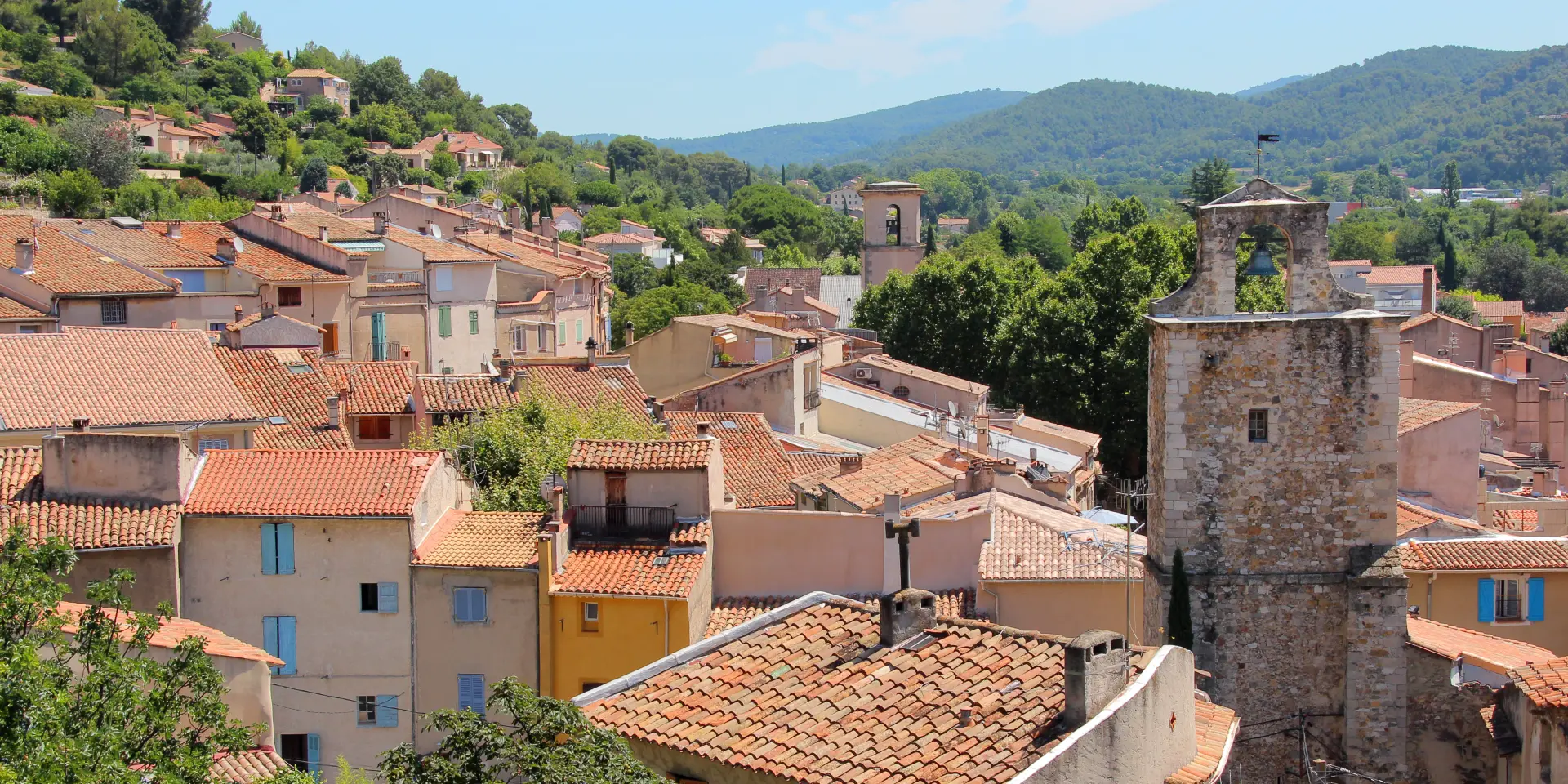 Panorama d’un village provençal d'Auriol avec toits en tuiles, tour en pierre et collines verdoyantes en arrière-plan.