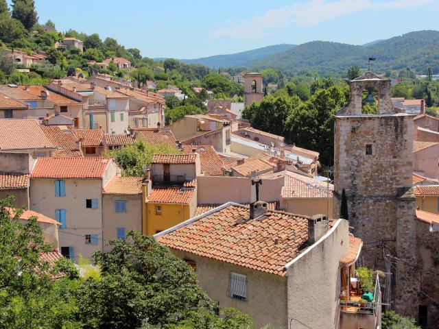 Panorama d’un village provençal d'Auriol avec toits en tuiles, tour en pierre et collines verdoyantes en arrière-plan.