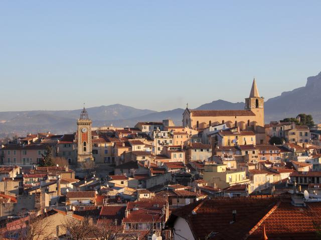 Vue panoramique d’Aubagne montrant les toits de la ville, l’église et la tour de l’Horloge, avec les montagnes en arrière-plan.