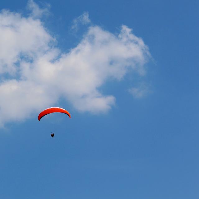 Parapentiste en vol sous un ciel bleu avec nuages blancs, voile de parapente orange visible en pleine altitude vers Aubagne