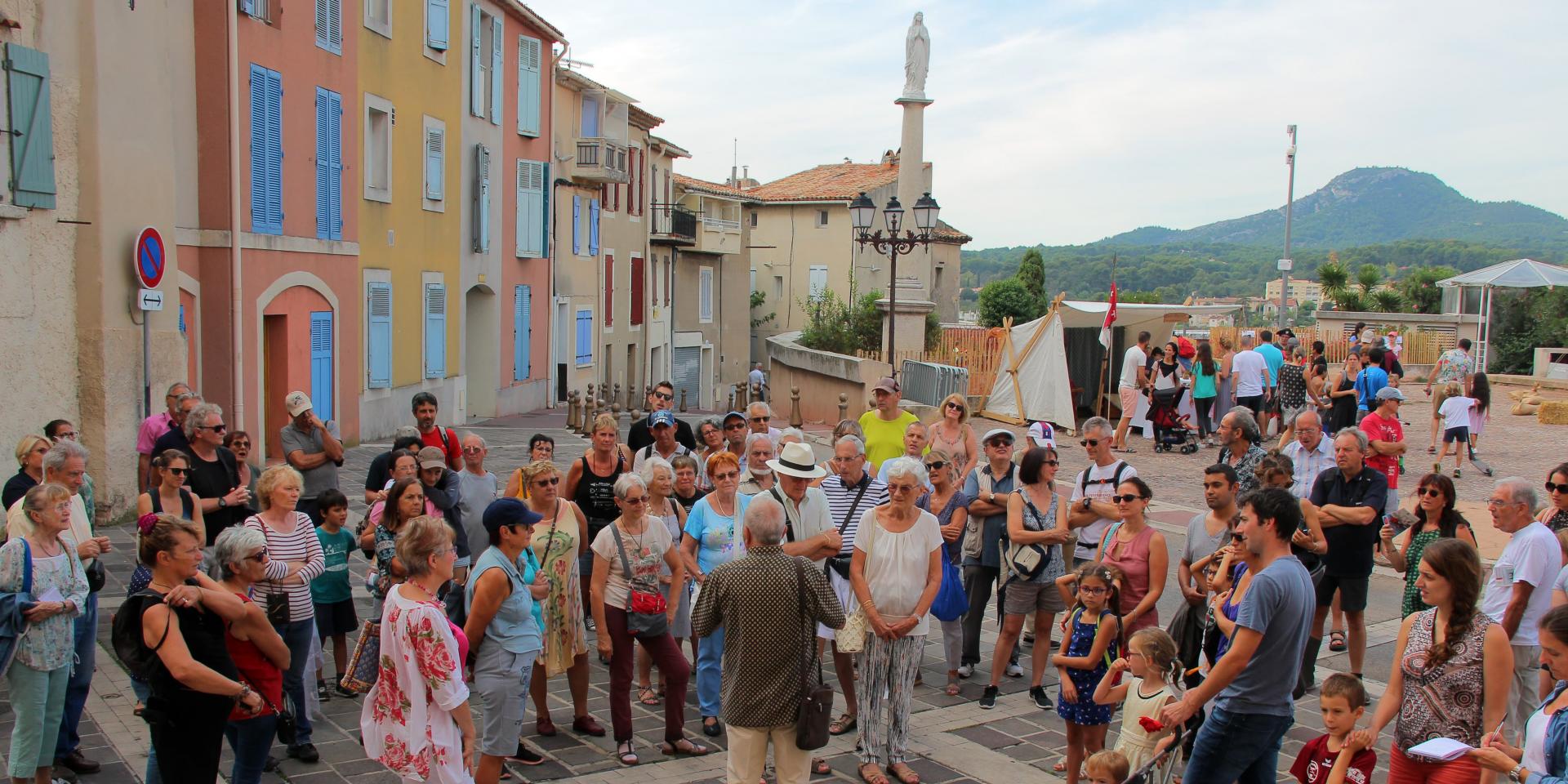 Groupe de visiteurs rassemblés autour d’un guide lors d’une visite touristique dans une rue pavée d’Aubagne.