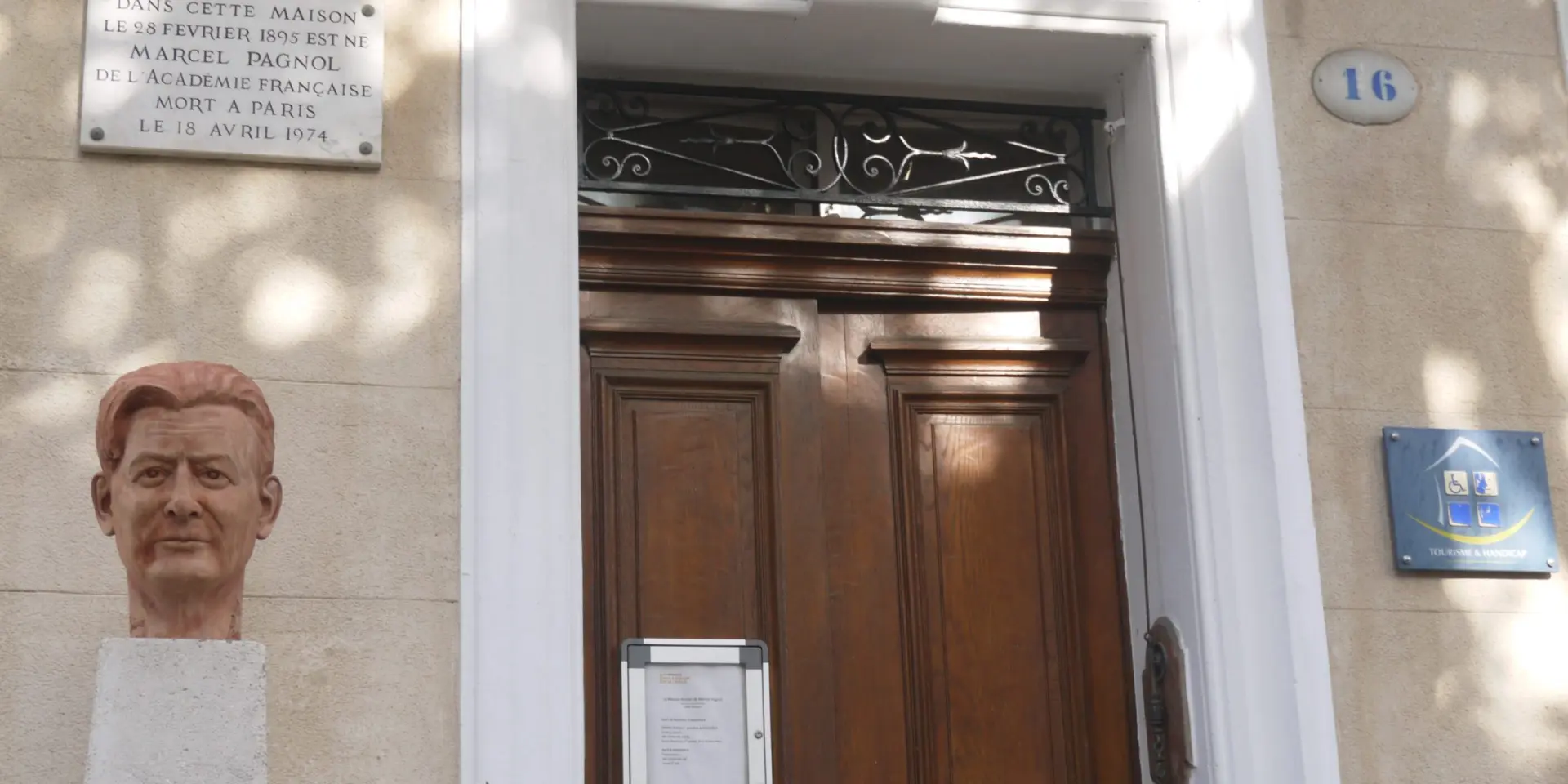 Façade de la maison natale de Marcel Pagnol à Aubagne avec porte en bois, plaques commémoratives et buste de l’écrivain.
