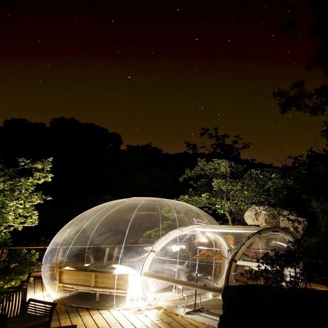 Bulle transparente éclairée la nuit, installée en pleine nature parmi les arbres, hébergement insolite sous le ciel nocturne - Bulle des Bois à Cuges-les-Pins