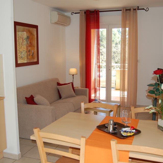 Séjour lumineux avec table à manger, cuisine ouverte, canapé, décoration moderne et porte-fenêtre donnant sur l’extérieur. Hébergement de résidence de tourisme à Peypin