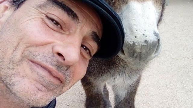 Homme souriant posant aux côtés d’un âne dans un environnement naturel au domaine de Font de Mai à Aubagne
