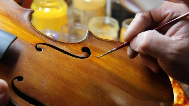 Main d’un luthier appliquant une retouche de vernis sur un violon à l’aide d’un pinceau fin