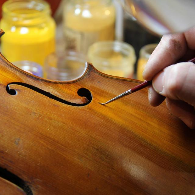 Main d’un luthier appliquant une retouche de vernis sur un violon à l’aide d’un pinceau fin