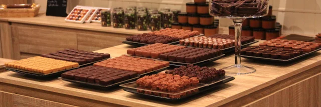 Table en bois présentant des plateaux de chocolats et confiseries artisanales dans une boutique à l’ambiance chaleureuse à la Biscuiterie et salon de thé chez Clément et Olivier