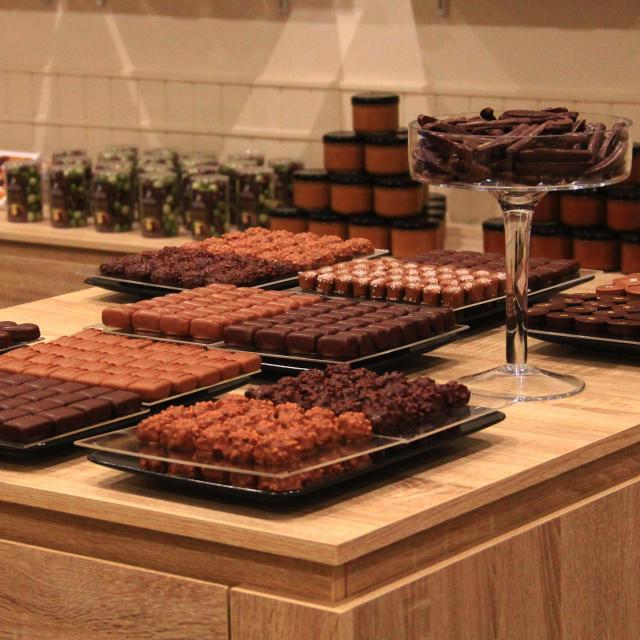 Table en bois présentant des plateaux de chocolats et confiseries artisanales dans une boutique à l’ambiance chaleureuse à la Biscuiterie et salon de thé chez Clément et Olivier
