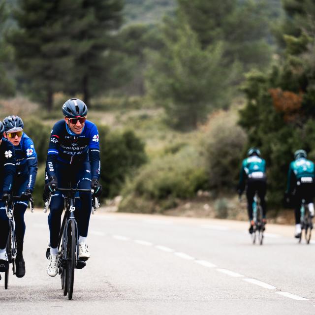 Groupe de cyclistes roulant sur une route entourée de végétation, deux à l’avant en tenue bleu foncé et deux autres plus éloignés en tenue verte à Aubagne