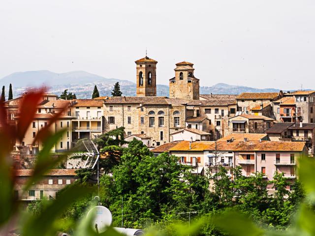 Vue sur la ville de Deruta avec ses bâtiments en pierre, ses toits orangés et ses deux clochers au-dessus d’une végétation verdoyante.