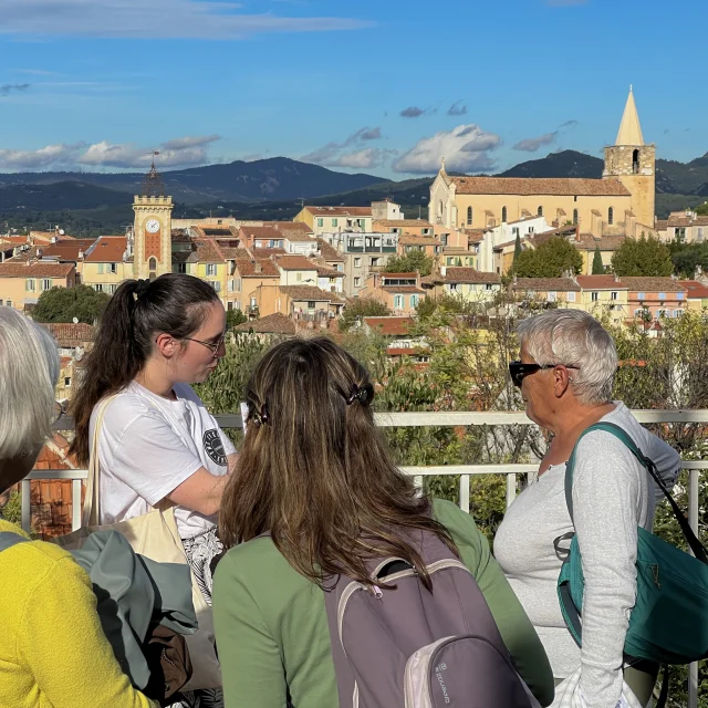 Groupe de personnes participant à une visite guidée, observant un village provençal avec église, clocher et maisons aux toits en tuiles en arrière-plan à Aubagne