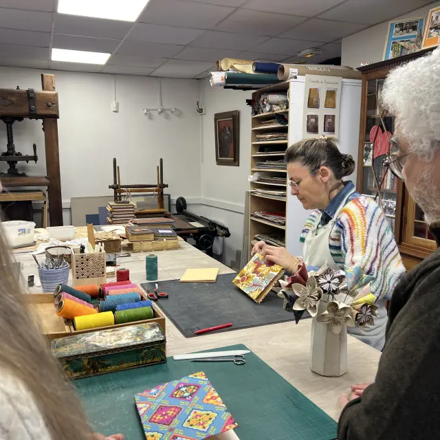 Personnes observant une relieuse artisanale travaillant sur la couverture d’un livre dans un atelier de reliure.