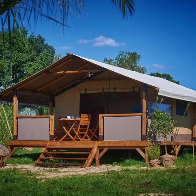 Hébergement de plein air type lodge en bois avec terrasse couverte, mobilier extérieur et vue sur un environnement naturel verdoyant au camping du Garlaban à Aubagne