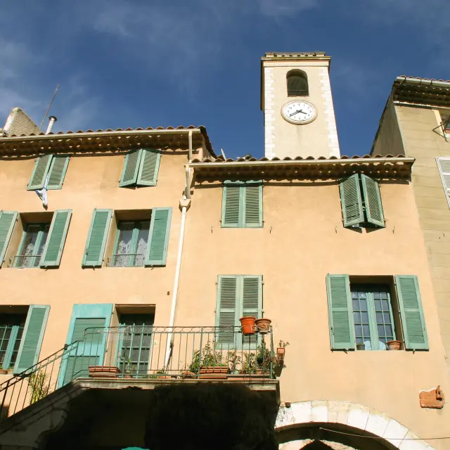 Maisons aux façades ocre avec volets verts et clocher d’église dans un village provençal sous un ciel bleu à Cuges-les-Pins
