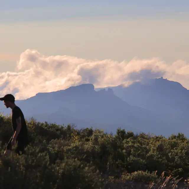 Randonneur marchant dans la garrigue du massif du Garlaban avec vue sur les reliefs montagneux et les nuages en Provence.